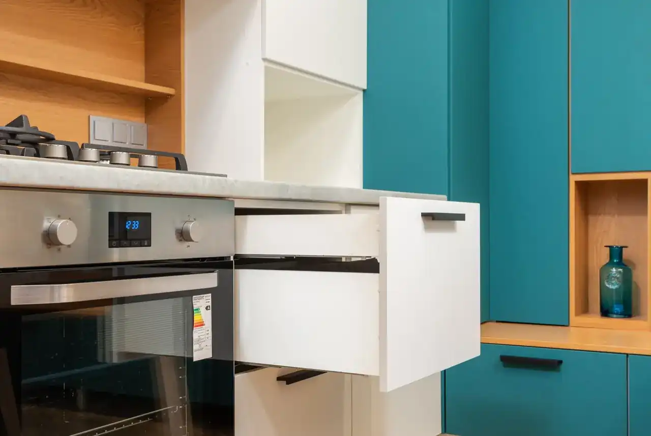 Cajon calientaplatos encastrable abierto bajo el horno con platos y tazas en una cocina moderna