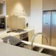 Persona descongelando un congelador en una cocina en verano, con escarcha, toallas y agua en el suelo mientras prepara la limpieza del aparato.