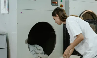 Persona doblando ropa frente a una lavadora de carga frontal que expulsa vapor, ilustrando Lavadoras con vapor para secar y cuidar mejor la ropa y el aspecto de la ropa fresca y cuidada.