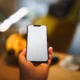Horno con cámara interior inteligente: cómo cambia la cocina conectada — mano sostiene un smartphone que muestra la vista interior del horno con alimento en la rejilla, en una cocina moderna.