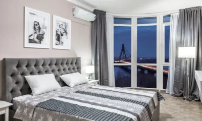 Mano pulsando el temporizador aire acondicionado en un mando a distancia, en un dormitorio por la noche con la cama y luz cálida de fondo