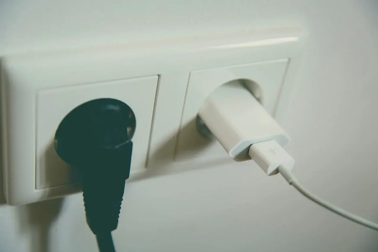 En una sala de estar, un televisor con luz de espera y varios enchufes conectados ilustra el consumo fantasma electrodomesticos.