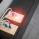 Mano desenchufando una regleta frente a un televisor con luz de standby roja, imagen para el artículo Qué electrodomésticos gastan más luz en standby y cómo evitarlo.