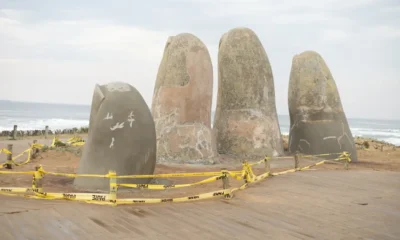 Mano pulsando el botón del modo turbo aire acondicionado en un mando a distancia, con la unidad split montada en la pared de un salón al fondo