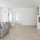 Salón moderno con mueble televisor blanco y madera junto a un sofá gris y luz natural.