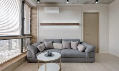 Persona ajustando el mando del aire acondicionado a 24°C en un salón con persianas bajadas, imagen para ilustrar ahorrar luz con electrodomésticos verano