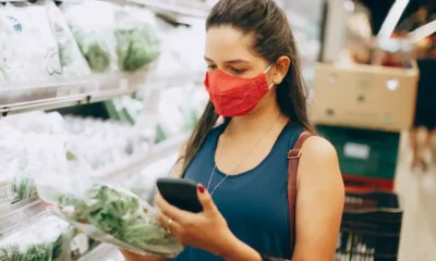 Persona consulta en el móvil una nevera que avisa caducidad alimentos mientras revisa los productos del frigorífico