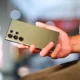 Persona en cocina moderna sosteniendo un smartphone que muestra la vista de la cámara interior de un horno con un pollo asado — imagen para el artículo Horno inteligente con cámara interior: funciones, ventajas y límites.