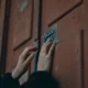 Persona desbloqueando una puerta moderna con el móvil, con foco en el canto de la puerta y la cerradura oculta — imagen para el artículo Cerraduras invisibles con Wi-Fi: claves para elegir bien