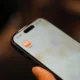 Persona sosteniendo un smartphone con la app del termostato frente a un aire acondicionado de pared, ilustración para 'Aire acondicionado inteligente sin internet: cómo funciona y límites'.