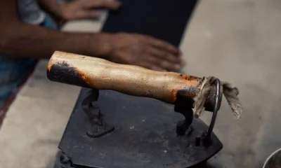 Imagen ilustrativa de como limpiar la plancha de la ropa quemada: una plancha con la suela manchada mientras una persona la limpia cuidadosamente con un paño en una mesa de trabajo.