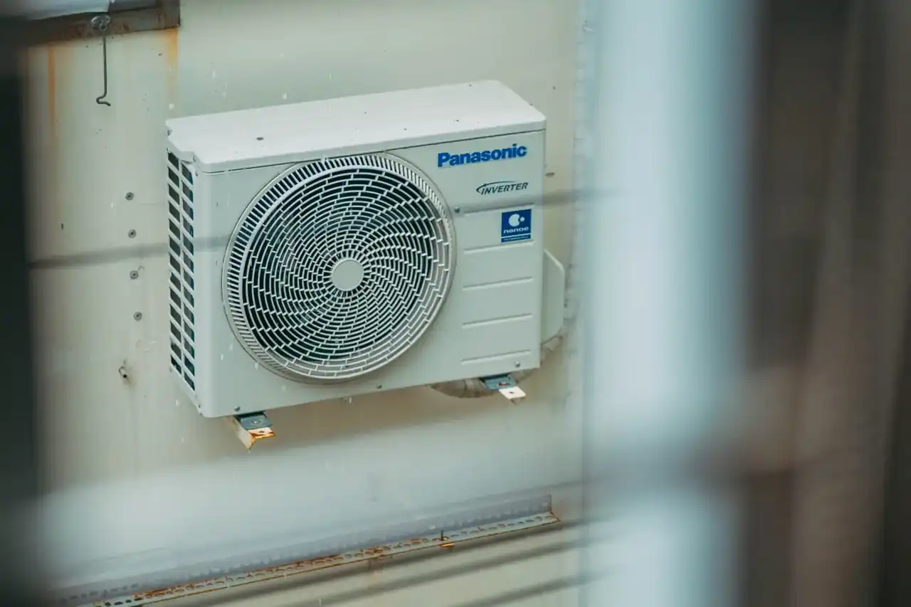 Persona junto a un aire acondicionado bomba de calor portatil con la manguera de evacuación instalada en la ventana y el mando en la mano, ilustrando consejos de compra — Aire acondicionado bomba de calor portatil: claves para elegir bien