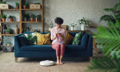 Robot aspirador en un salón junto a un sofá mientras una persona consulta reseñas en el móvil — Robot aspirador Lidl Silvercrest: opiniones y análisis real