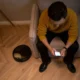 Persona sosteniendo un smartphone con la app del robot aspirador abierta mientras un robot Xiaomi limpia el suelo, ilustrando el artículo App para robot aspirador Xiaomi: funciones, conexión y límites.