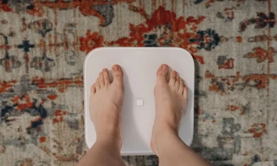 Mujer utilizando una bascula inteligente composicion corporal en el baño mientras consulta sus métricas en el móvil