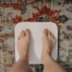 Mujer utilizando una bascula inteligente composicion corporal en el baño mientras consulta sus métricas en el móvil