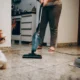 Persona utilizando un aspirador escoba friegasuelos en seco y humedo sobre el suelo duro de la cocina.